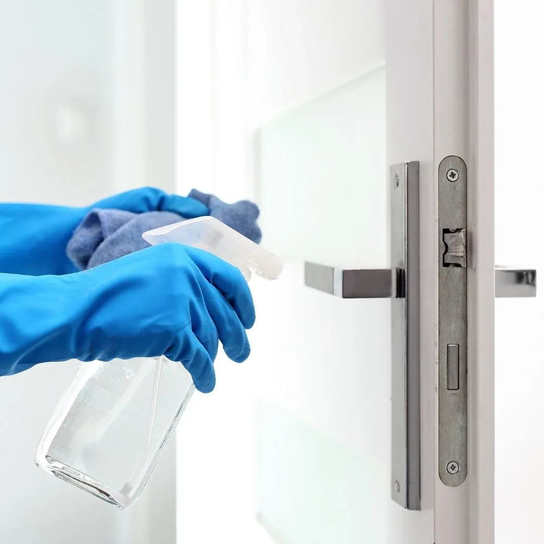 Cleaning professional spraying disinfectant on a door handle for a Greenville business Cleaning professional spraying disinfectant on a door handle for a Greenville business