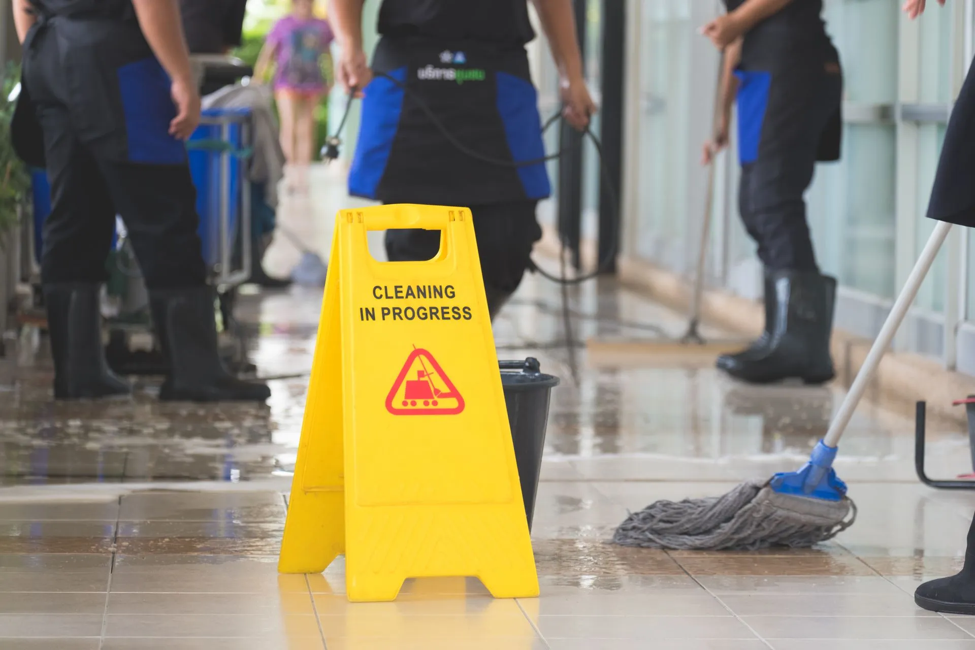 A group of cleaners are cleaning a floor with a yellow caution sign. A group of cleaners are cleaning a floor with a yellow caution sign.