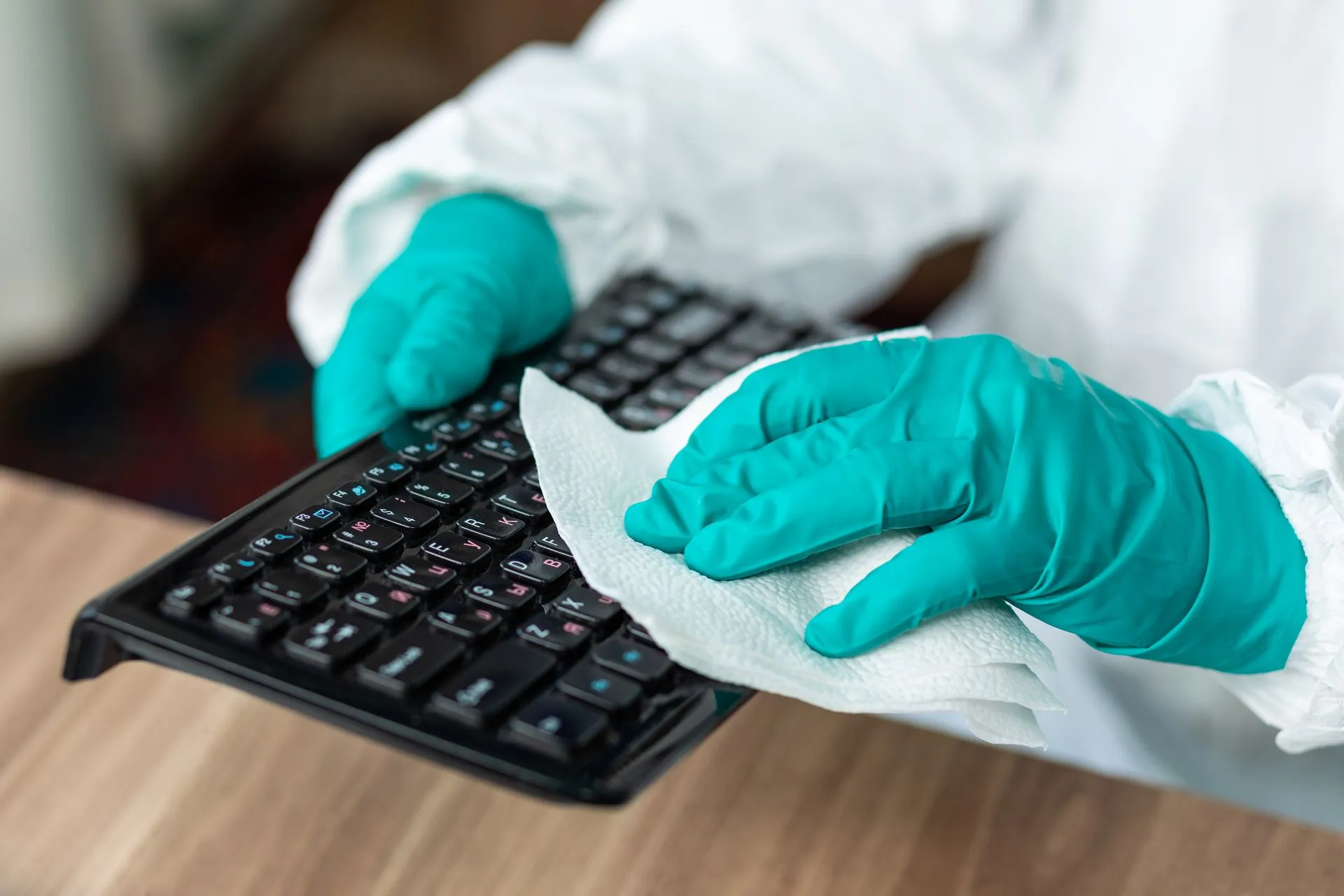 A person wearing gloves is cleaning a keyboard with a napkin. A person wearing gloves is cleaning a keyboard with a napkin.
