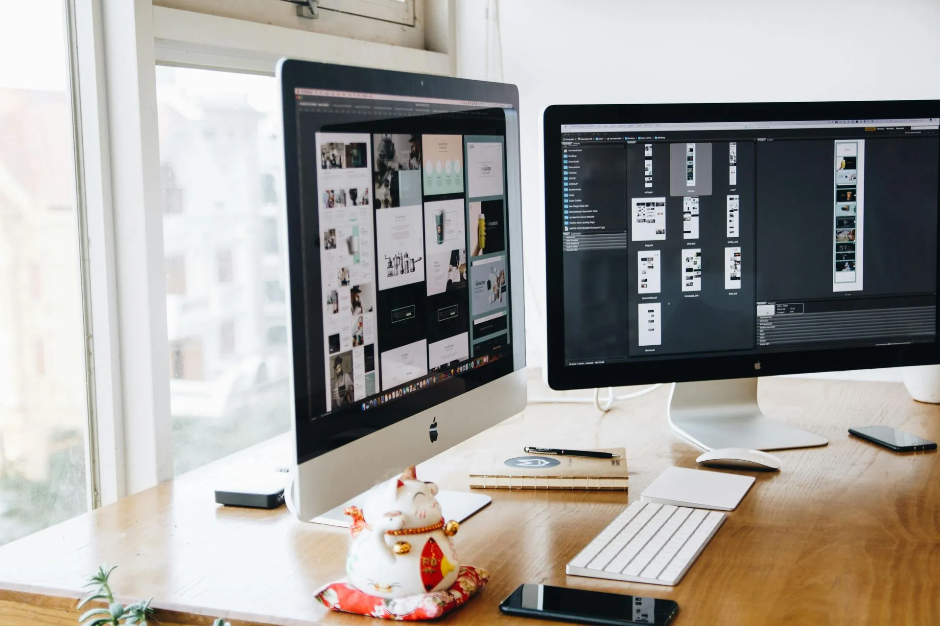 Two computer monitors are sitting on a wooden desk next to a window.